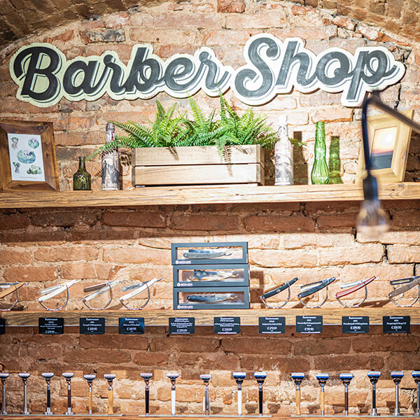 Text: Innenraum aus Ziegelsteinoptik Barbershop, ausgestattet mit Rasier-Messer, Blumentopf, verschiedene Glasflaschen.